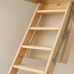 Close-up of a wooden loft ladder with metal hinges against a neutral wall